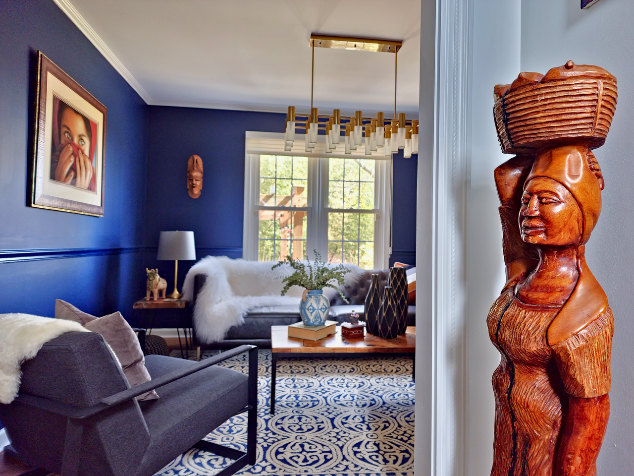 a wooden statue stands in the middle of a blue living room design by bespoke by ali fasi main line philadelpha